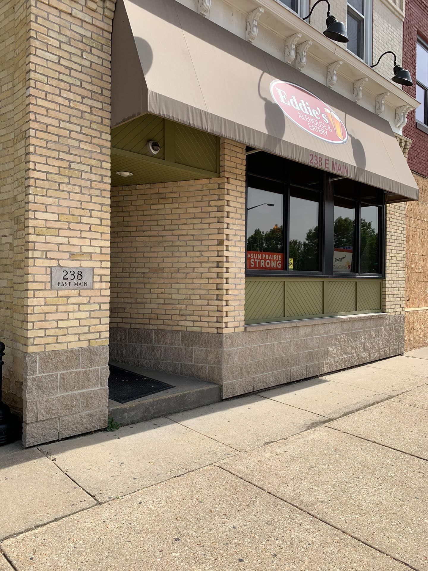 The exterior of a brick building with a tan awning, a sign reading "238 E Main," and a window sign that says "Funpare Strong.
