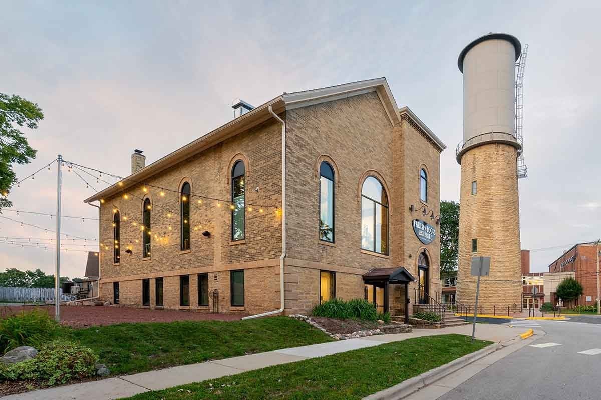 A two-story brick building with arched windows sits next to a tall water tower; string lights hang across the small outdoor area.