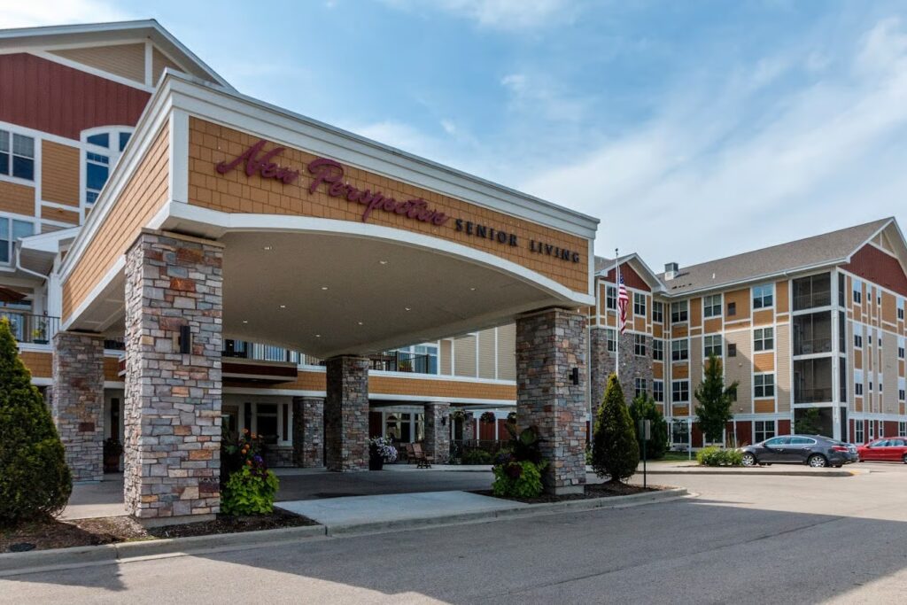 Entrance of a multi-story senior living facility with stone pillars, tan and red siding, and the sign “New Perspective Senior Living” above the covered driveway.