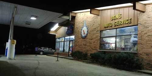 Exterior view of Ben's Auto Service at night, showing illuminated windows, a clock sign, and a pickup truck parked outside.