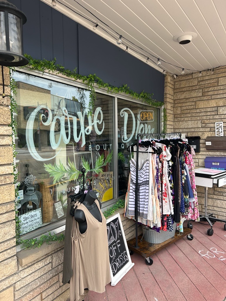 Clothing racks with dresses are displayed outside a boutique with a sign reading "20% off dresses" in front of a large window labeled "Carve Don Boutique.