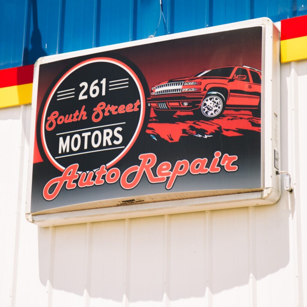 A rectangular sign reads "261 South Street Motors Auto Repair" with an illustration of a red pickup truck against a black and red background.